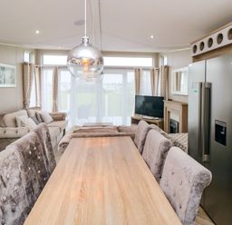 A dining table with upholstered chairs a sofa a television and a refrigerator in a living room at Finch 65 in Cayton Bay