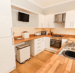 A kitchen with white cabinets wooden countertops a stainless steel sink gas stove oven toaster and mounted television at Grace House in Silloth