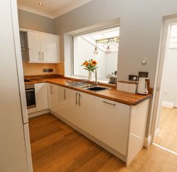 A kitchen with white cabinets wooden countertops a sink and a window with flowers at Grace House in Silloth