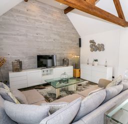 A living room with a gray sofa a glass coffee table and a TV on a white cabinet at The Bit on the Side in Ettington
