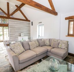 A living room with a gray sectional sofa and wooden beams on the ceiling at The Bit on the Side in Ettington