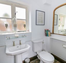 A bathroom with a sink toilet mirror and window with decorative items at The Bit on the Side in Ettington