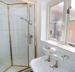 A bathroom with a shower enclosure a sink with dual taps and candles on the windowsill at The Bit on the Side in Ettington