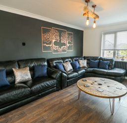 A living room with a black leather sectional sofa with pillows and a wooden round coffee table at Ty Copr in Amlwch