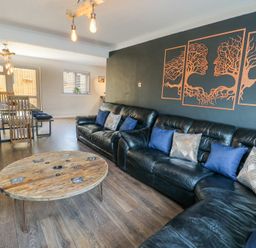 A living room with black leather sofas and a round wooden coffee table and a wooden dining table with chairs at Ty Copr in Amlwch