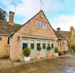 A stone house with green doors and potted plants outside at The Elm Coach House in Chipping Norton