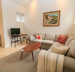A living room with a beige sectional sofa a wooden coffee table a TV on a stand and paintings on the walls at The Elm Coach House in Chipping Norton