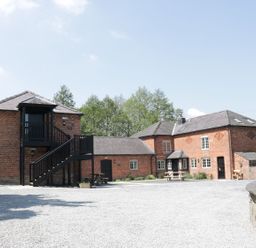 A gravel courtyard with brick buildings and black wooden staircases surrounded by trees at Woodside Cottage in Kerry