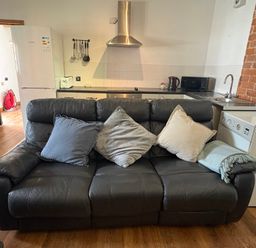 A living room with a sofa in front of a kitchen at Woodside Cottage in Kerry