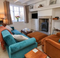 A living room with a teal sofa and orange armchair facing a wood stove and a window with flowers on the sill at Field View in Ruswarp