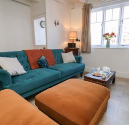 A living room with a teal sofa and orange ottomans near a window with flowers on a wooden coffee table at Field View in Ruswarp