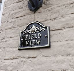 A black and white house nameplate saying Field View mounted on a beige stone wall next to a window at Field View in Ruswarp