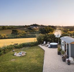 A garden with a fire pit a hot tub loungers and a small cabin near fields at Stargazer in St Erme near Truro