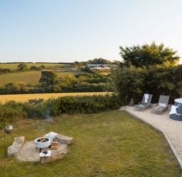 A garden with a fire pit surrounded by stones loungers and a hot tub on a gravel area at Stargazer in St Erme near Truro