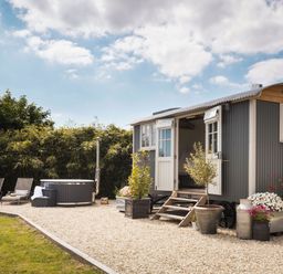 A small cabin with open doors and stairs in a garden with plants and lounge chairs near a hot tub at Stargazer St Erme near Truro