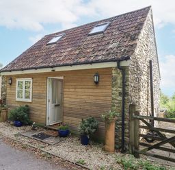 A small house with stone and wood exterior a tiled roof and potted plants outside at The Wheelhouse Beacon near Yarcombe