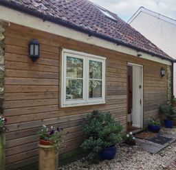 The exterior of a wooden house with a window and an open door with potted plants along a gravel path at The Wheelhouse in Beacon near Yarcombe