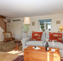 A living room with a gray sofa and red cushions a wooden chest used as a coffee table a wicker chair and staircase at The Wheelhouse Beacon near Yarcombe