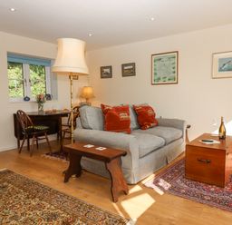 A living room with a gray sofa red cushions wooden coffee table and a dining table by the window at The Wheelhouse Beacon near Yarcombe