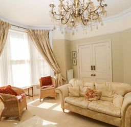 A sitting room with a fabric sofa and two wicker chairs near windows with curtains at Hereford House in Tenby