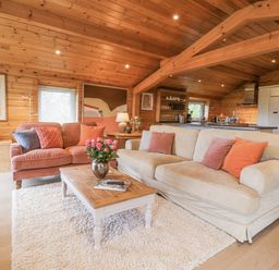 A living room with two sofas a wooden coffee table with flowers and a kitchen area at Artisan Lodge in Longridge
