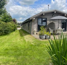 A wooden lodge with patio furniture and umbrella on a deck surrounded by grass and potted plants at Artisan Lodge in Longridge