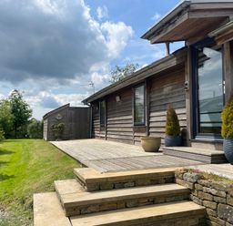 An exterior view of a wooden house with steps leading to a wooden deck and plants in pots at Artisan Lodge in Longridge