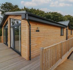 A wooden cabin with large glass doors and a wooden deck surrounded by trees at Bay in Ilfracombe