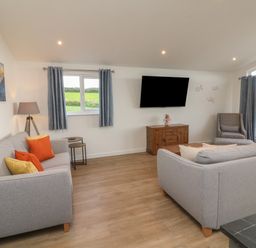 A living room with two gray sofas, a wooden cabinet with a TV mounted above it, a patterned armchair, and windows with blue curtains at Bay in Ilfracombe