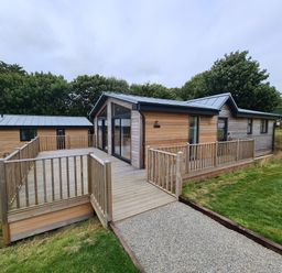 A wooden lodge with large glass doors and a fenced wooden deck surrounded by grass at Cove Lodge in Ilfracombe