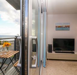 A balcony with a wooden table and two glasses overlooking the sea and a living room with a TV on a stand and a floor lamp at 7 Warren Edge Close in Bournemouth