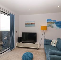 A living room with a blue sofa a television on a stand a yellow floor lamp and sliding glass doors leading to a balcony at 7 Warren Edge Close in Bournemouth