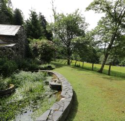 A garden with a stone pond and trees beside a stone building at Beaver Grove Cottage in Betws-Y-Coed