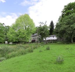 A grassy field with trees and a stone building in the background at Beaver Grove Cottage in Betws-Y-Coed