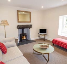 A living room with a sofa a fireplace a TV on a small table a round coffee table and a red plaid bench at Beaver Grove Cottage in Betws-Y-Coed