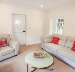 A living room with armchair and sofa with red checkered cushions and a round coffee table at Beaver Grove Cottage in Betws Y Coed