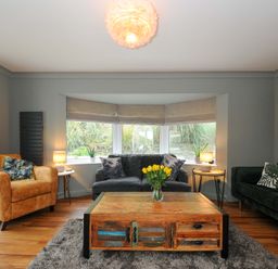 A living room with a yellow armchair gray sofa green velvet couch wooden coffee table and three windows at Waves Edge in Looe
