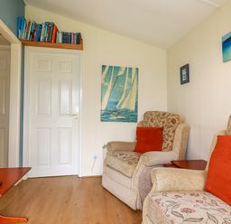 A sitting room with two armchairs a small television on a table and books above a door at Fox Cove near St Merryn