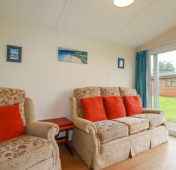 A living room with floral patterned sofas and red cushions next to a glass door at Fox Cove near St Merryn