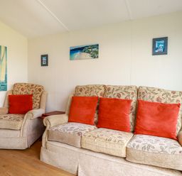 A living room with a floral sofa and armchair with red cushions and paintings on the wall at Fox Cove near St Merryn