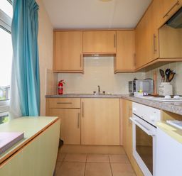 A kitchen with wooden cabinets a sink a stove a microwave and a window with blue curtains at Fox Cove near St Merryn