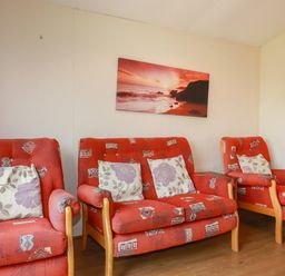 A living room with red patterned chairs and a red sunset picture on the wall at Pepper Cove near St Merryn