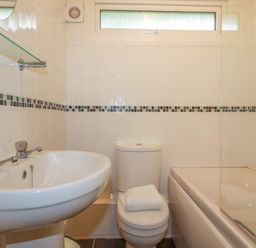 A bathroom with a sink a toilet with a towel on it and a bathtub with tiled walls at Pepper Cove near St Merryn