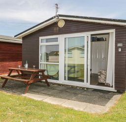 A small wooden cabin with a picnic table outside on a paved area at Warren Cove near St Merryn