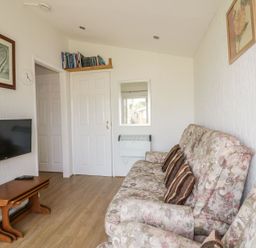 A living room with patterned sofas a wall-mounted television and a small wooden table at Warren Cove near St Merryn