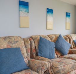 A living room with patterned sofas and blue cushions below beach-themed wall art at High Cove near St Merryn