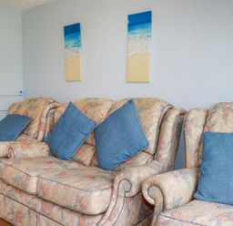 A living room with floral sofas and blue cushions under beach paintings at High Cove near St Merryn