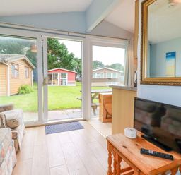 A living room with a floral armchair a wooden table with a TV and remote control glass sliding doors opening to a garden at High Cove near St Merryn