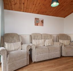 A sitting room with three beige armchairs and a beach photo on the wall at Hawkers Cove near St Merryn