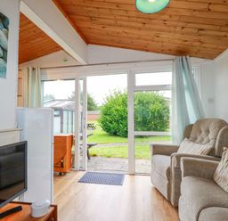 A living room with armchairs a television and glass doors opening to a garden at Hawker's Cove near St Merryn